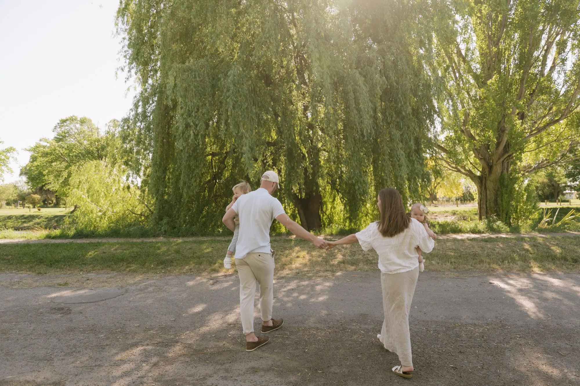 A young family walking hand in hand beneath willow trees