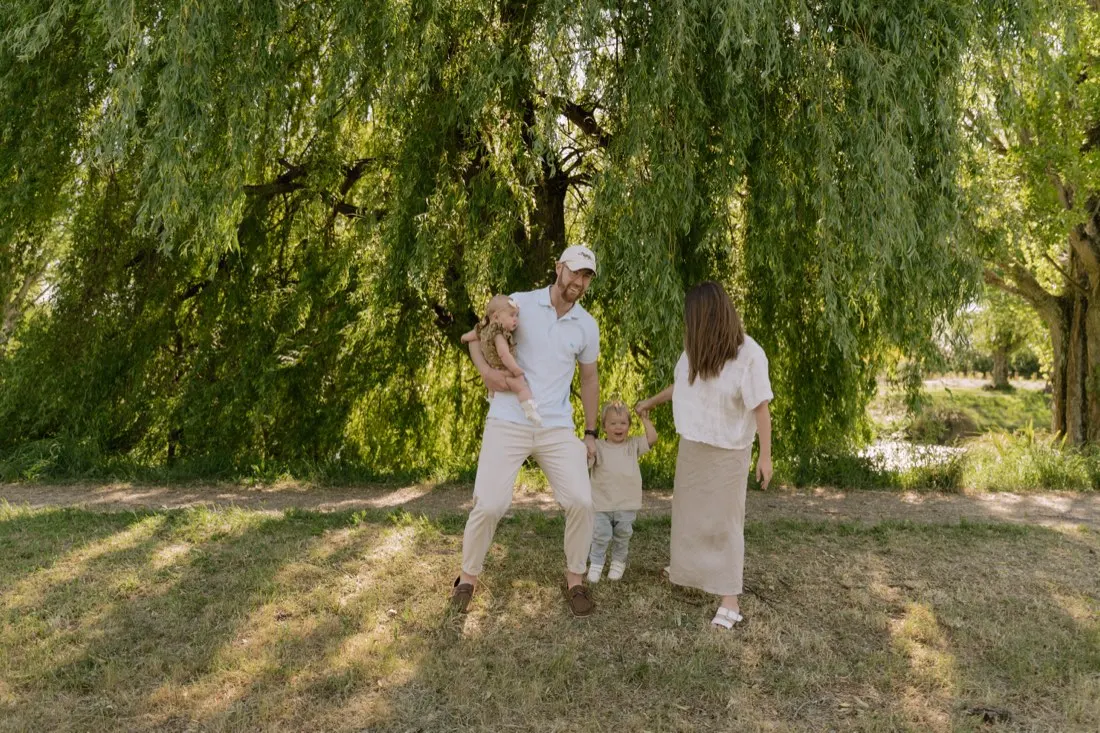 Parents walking hand in hand with their toddler beneath a willow tree