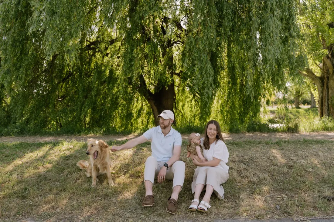 A young family sitting with their golden retriever beneath a willow tree
