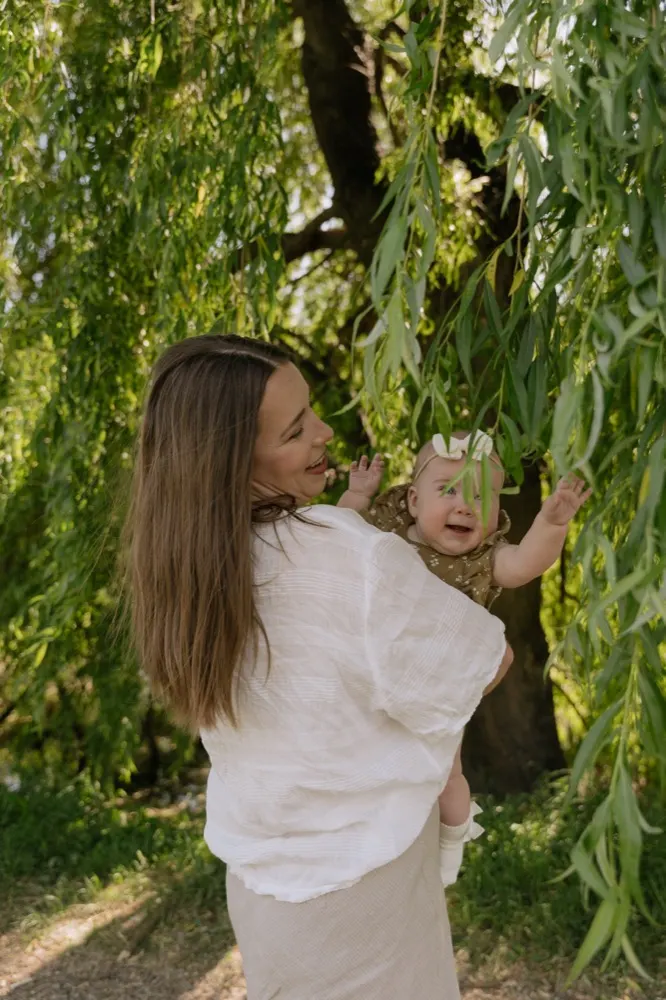 A mother laughing with her baby among willow branches