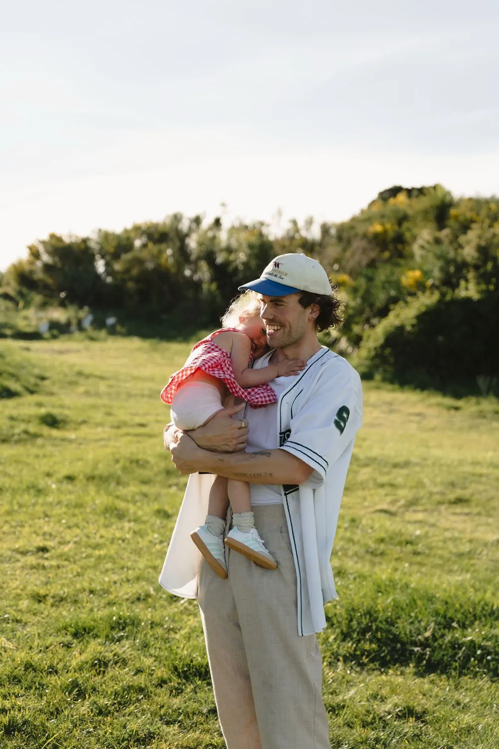 A father holding his young daughter in a sunlit Christchurch field