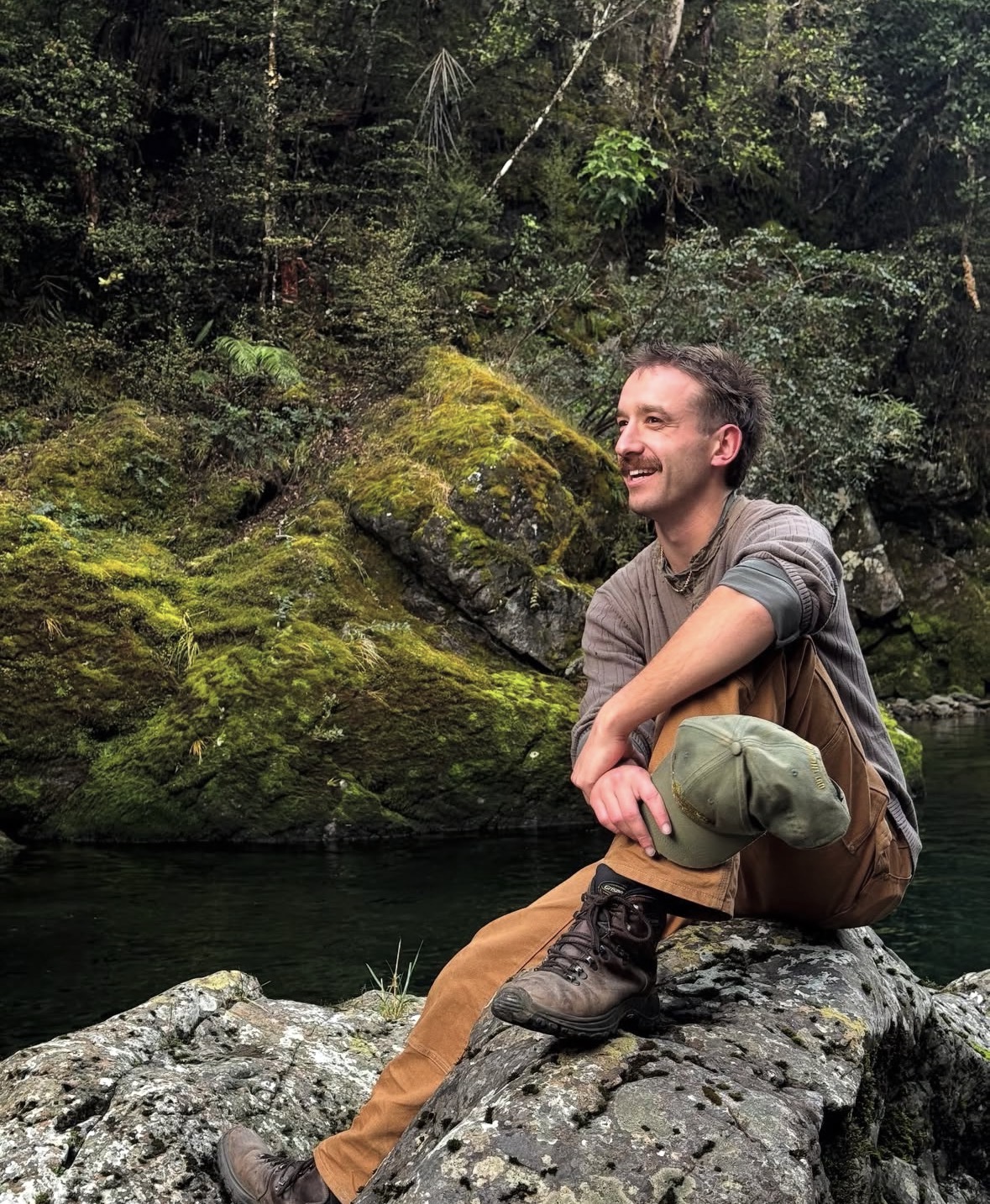 Harrison O'Connor sitting by a river in the New Zealand bush
