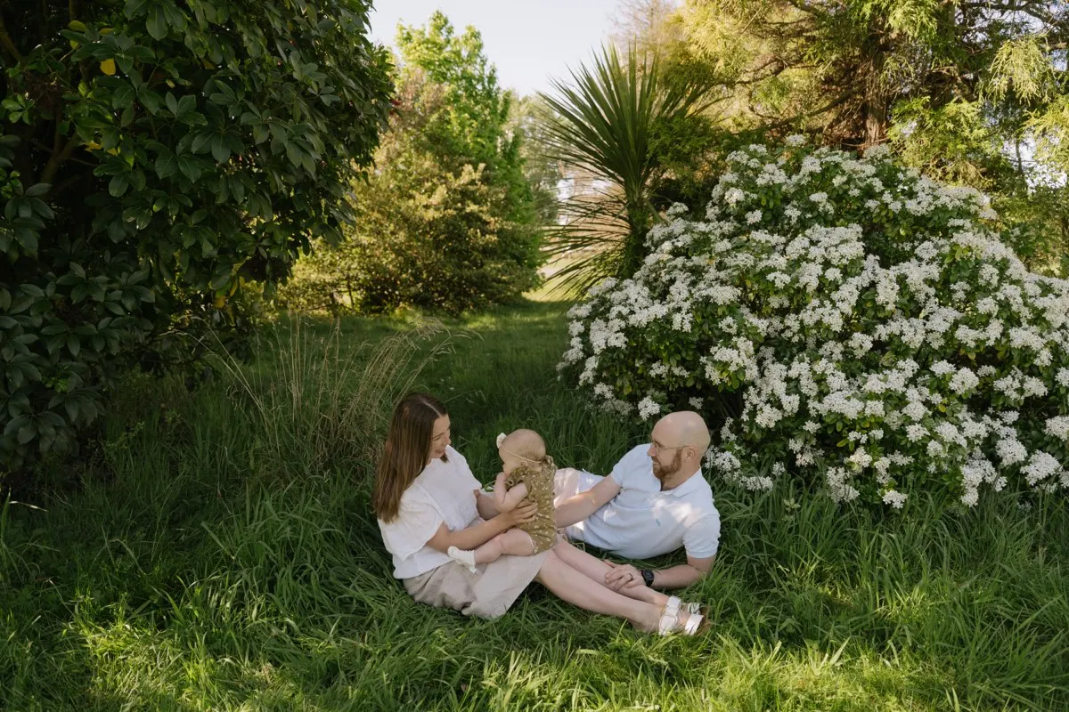 A young family relaxing together in long grass beside white blossoms